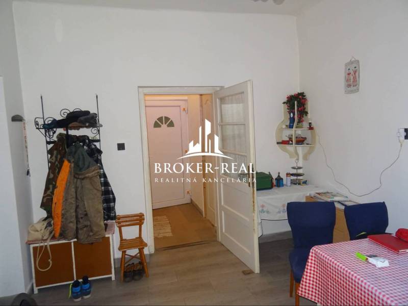 Családi ház belső tere fa dekorációjú padlóval, étkezőasztallal és ruhafogassal.