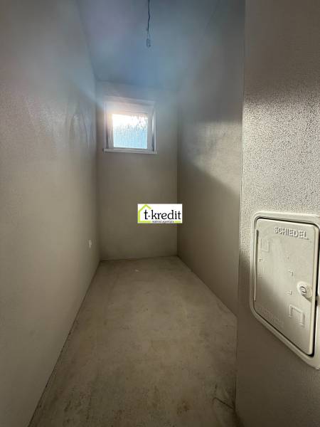 Úzka tárolóhelyiség egy családi házban ablakkal és betonpadlóval.