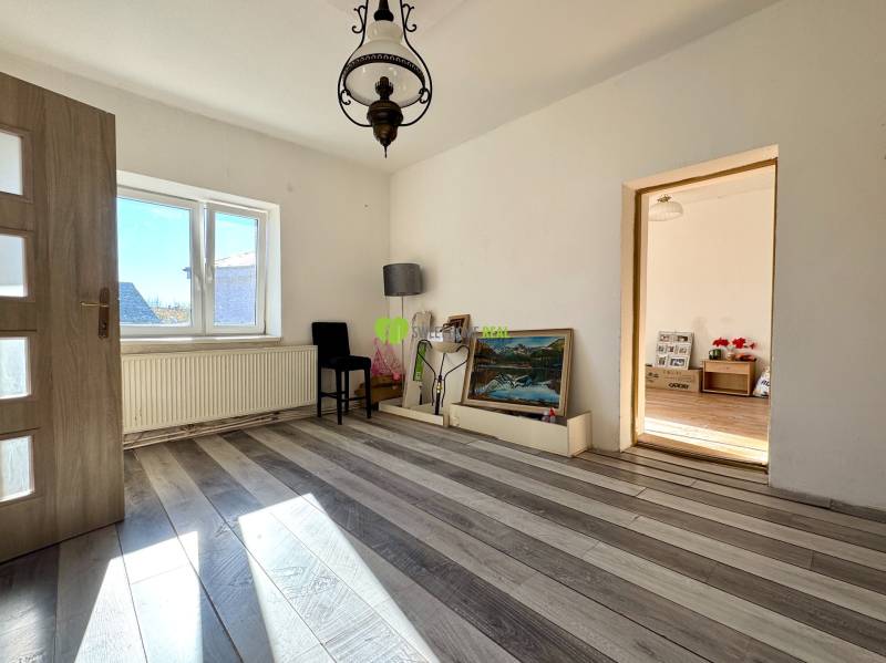 Egy családi ház szobája fehér falakkal, fa mintázatú padlóval és nagy ablakkal.