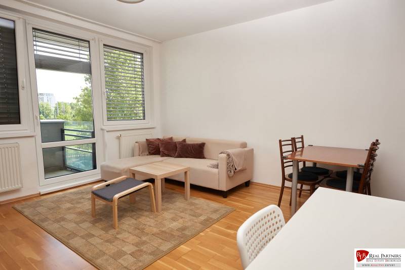 Nappali kanapéval, étkezőasztallal és fa dekorációjú padlóval egy kétszobás lakásban.