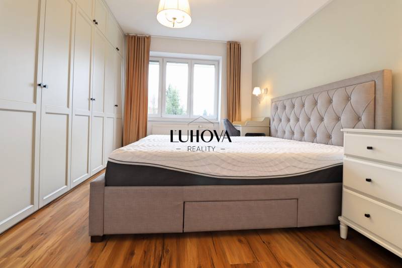 Világos hálószoba nagy ággyal, beépített szekrénnyel és fa dekorációjú padlóval egy háromszobás lakásban.