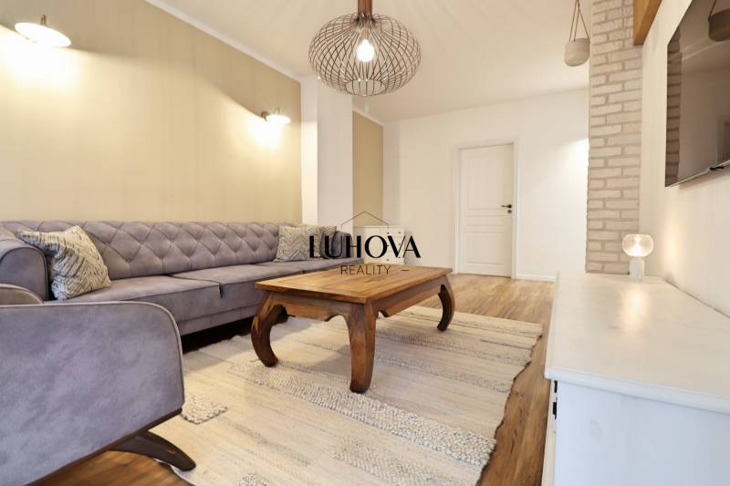 Nappali egy háromszobás lakásban kanapéval, fa asztallal és fa dekorációjú padlóval.