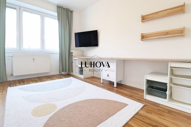 Szoba egy háromszobás lakásban, televízióval, fehér bútorokkal és fa dekorációjú padlóval.