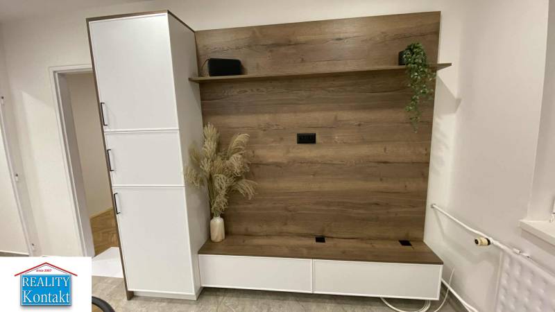 Az egyszobás lakásban van egy fa dekorációjú gardróbszekrény és egy váza virágokkal.