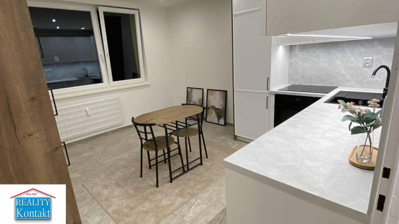 Konyha egy egyszobás lakásban étkezőasztallal, szekrényekkel és dekoratív képekkel a falon.