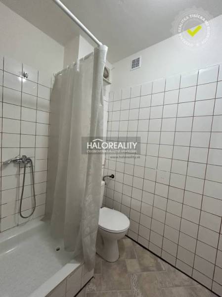 Fürdőszoba fehér csempékkel és zuhanyzóval egy egyszobás lakásban.