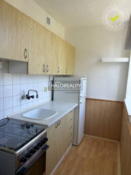 Konyha egy egyszobás lakásban fa szekrényekkel, tűzhellyel és fehér hűtőszekrénnyel.