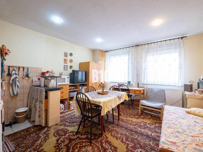 Szoba egy kétszobás lakásban szőnyeggel, asztallal, székkel és televízióval.