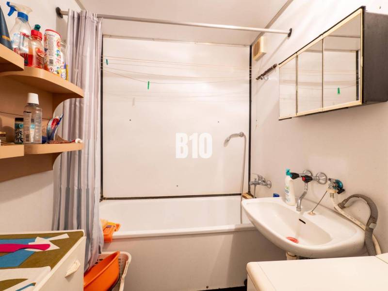 Fürdőszoba egy kétszobás lakásban káddal és tisztítószerekkel ellátott polccal.