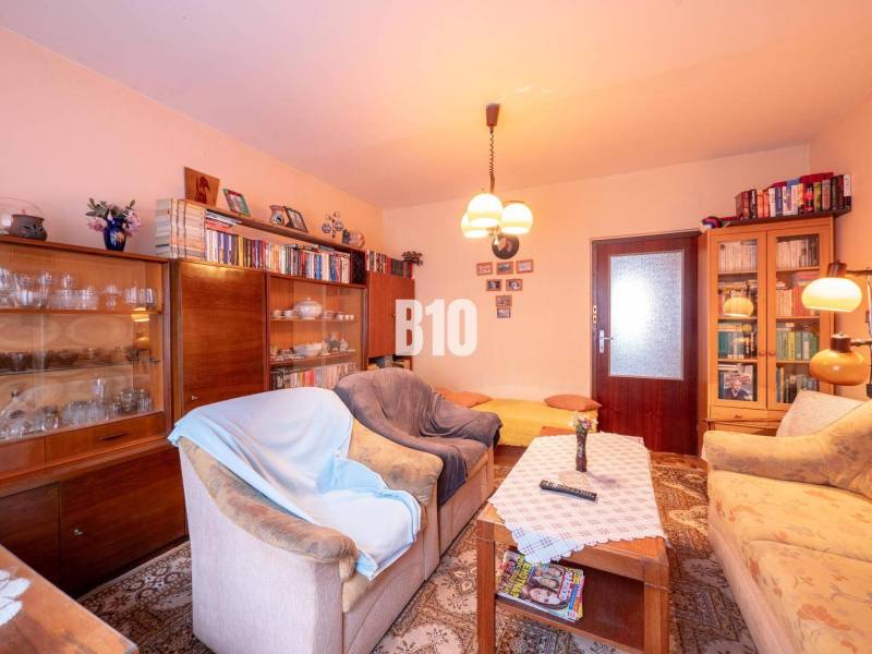 Nappali egy kétszobás lakásban kanapékkal, könyvespolccal és fa dekorációjú padlóval.