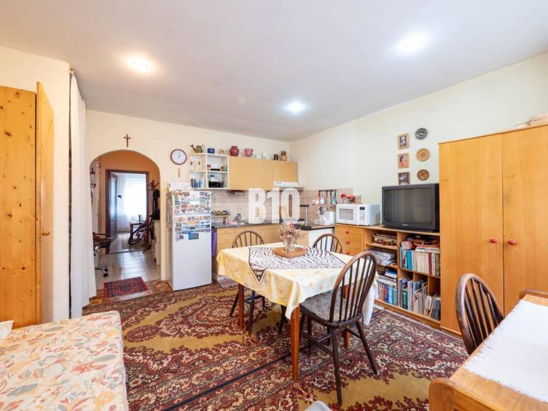 Konyha étkezőasztallal, szekrényekkel, szőnyeggel és televízióval egy kétszobás lakásban.