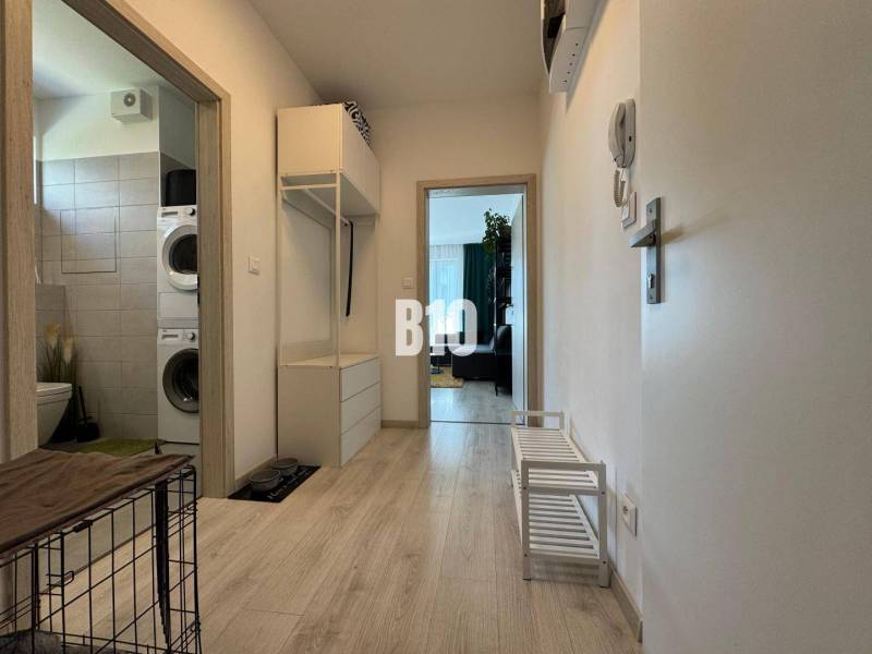 Folyosó egy kétszobás lakásban, fa dekoros padlóval, kilátás a fürdőszobába mosógéppel.