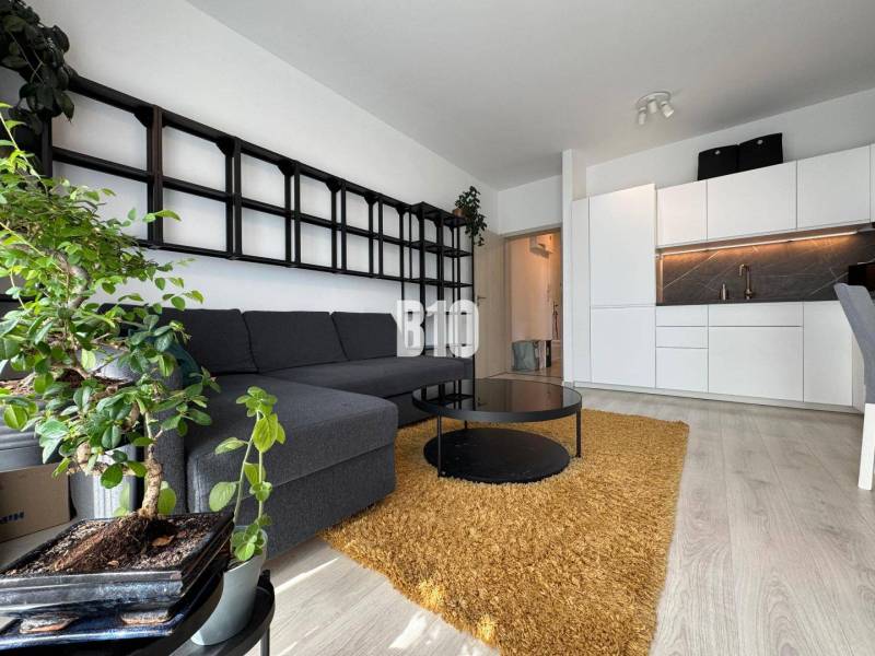 Nappali egy kétszobás lakásban kanapéval, asztallal és fa dekorációjú padlóval.