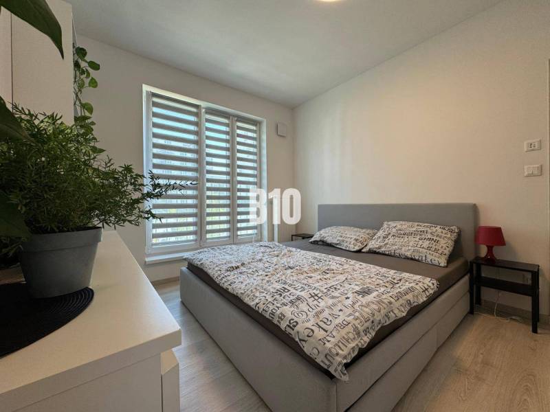 Hálószoba egy kétszobás lakásban ággyal, növénnyel és fa dekorációjú padlóval.