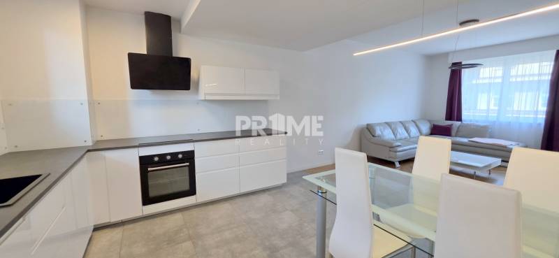 Konyha és nappali egy kétszobás lakásban, fa mintázatú padlóval és szürke kanapéval.