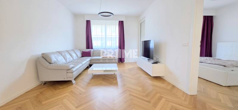 Világos nappali bőrkanapéval, TV-vel és fa mintázatú padlóval egy kétszobás lakásban.