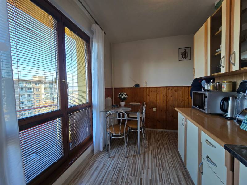 Konyha egy kétszobás lakásban fa hatású padlóval, nagy ablakokkal, étkező sarokkal.