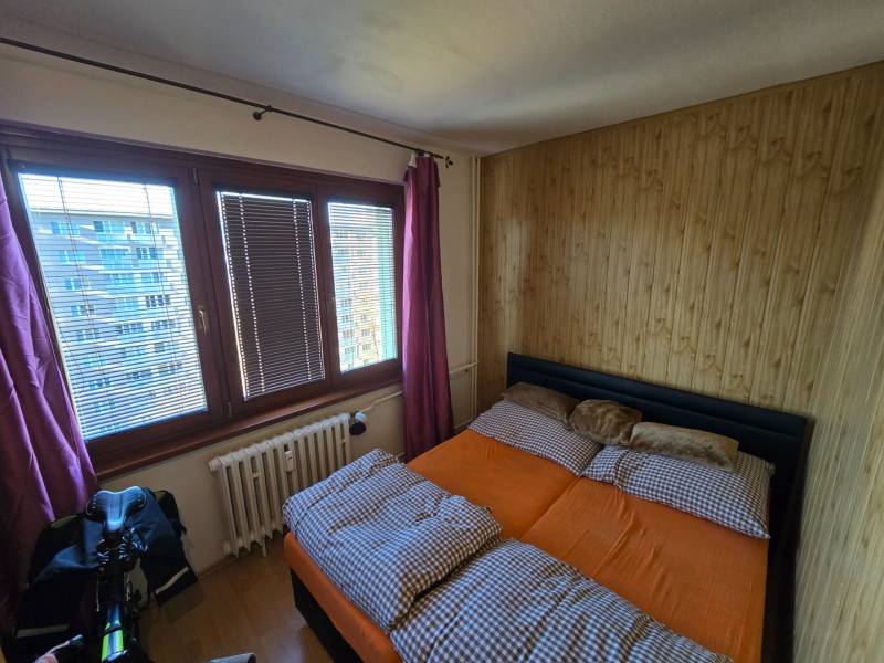 Hálószoba egy kétszobás lakásban ággyal és fa dekorációval a falon.