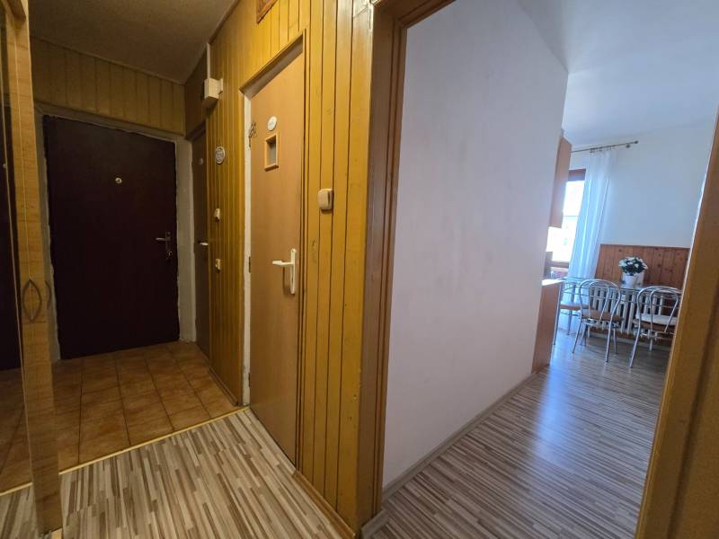 Csempefolyosó, fa dekor padló, kilátás egy kétszobás lakás konyhájába.