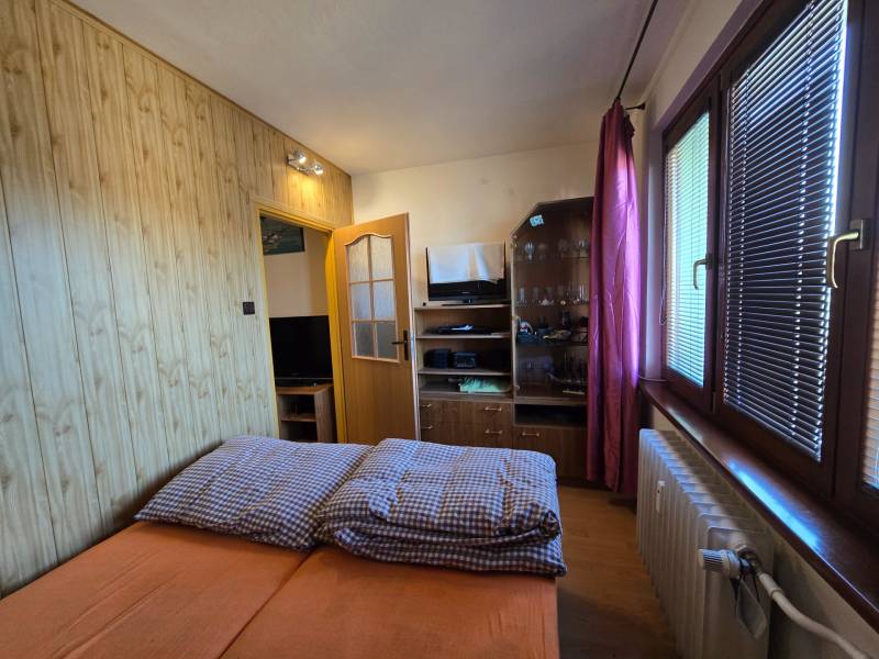 Hálószoba egy kétszobás lakásban, fa dekor padlóval, ággyal és tárolóegységgel.