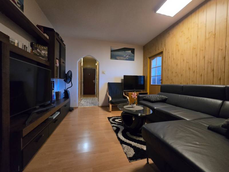 Nappali egy kétszobás lakásban, fa mintázatú padlóval és fekete kanapéval.