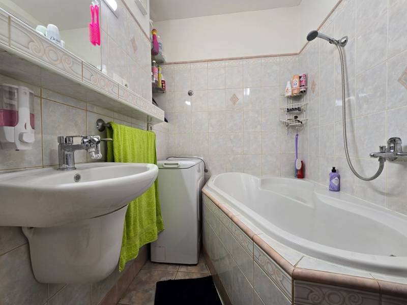 Fürdőszoba egy kétszobás lakásban mosdóval, káddal és mosógéppel, világos csempékkel kiegészítve.