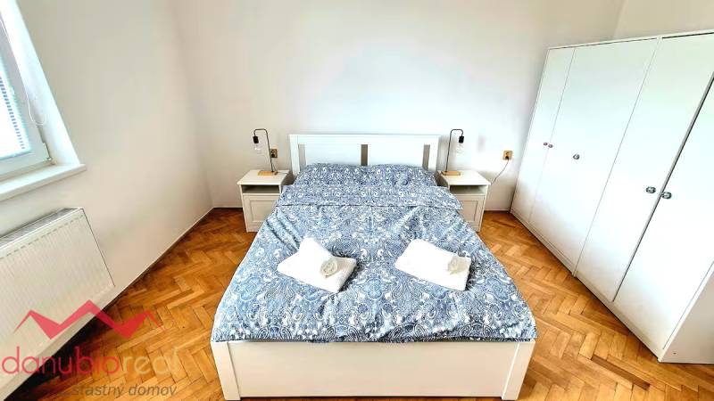 Hálószoba egy háromszobás lakásban ággyal, szekrényekkel és fa dekorációjú padlóval.