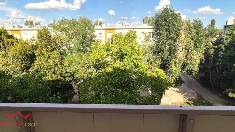 Kilátás egy háromszobás lakás erkélyéről Komáromban, fákkal és panelházakkal körülvéve.