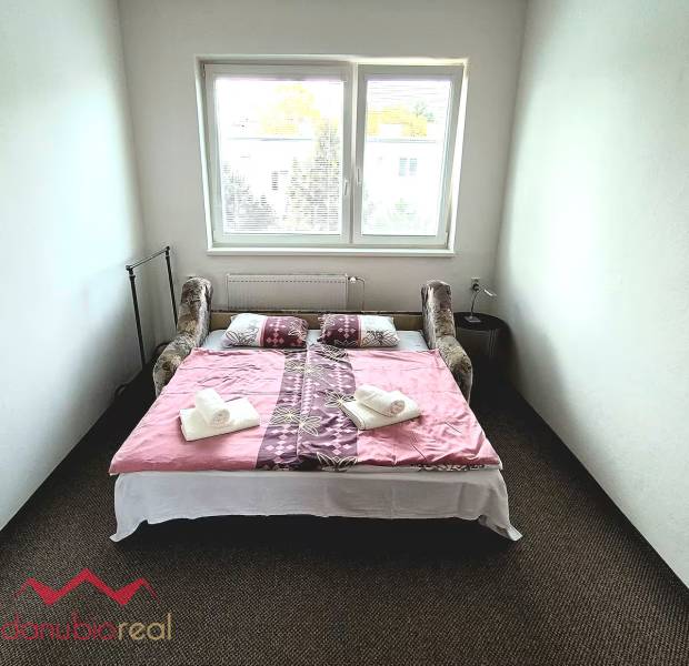 Hálószoba egy háromszobás lakásban ággyal, ablakkal és dekorációra helyezett törölközőkkel.