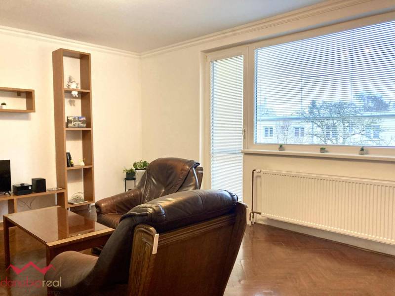 Nappali egy háromszobás lakásban, fa dekoros padlóval, nagy ablakkal és bőr fotelekkel.