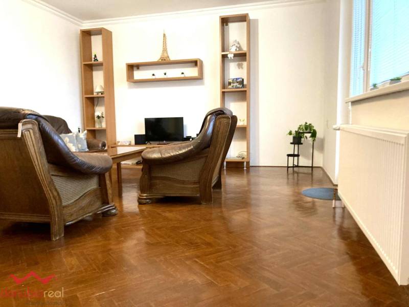 Nappali egy háromszobás lakásban bőr fotelekkel és fa dekorációjú padlóval.