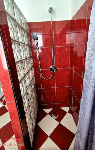 Zuhanykabin piros csempékkel és üvegfallal egy háromszobás lakásban.