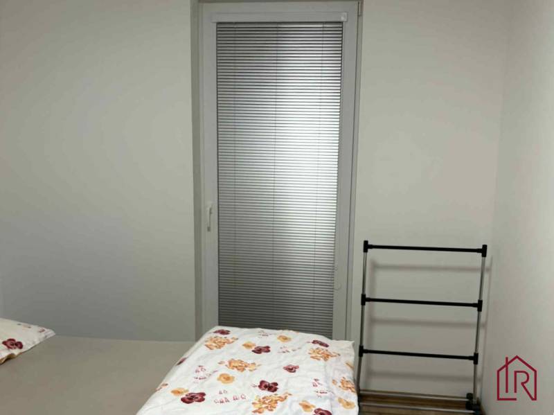 Hálószoba egy kétszobás lakásban erkélyajtóval, ággyal és ruhaszárítóval.