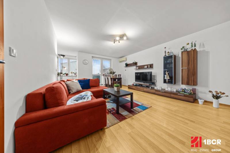 Nappali egy kétszobás lakásban, fa dekoros padlóval, kanapéval és televízióval.