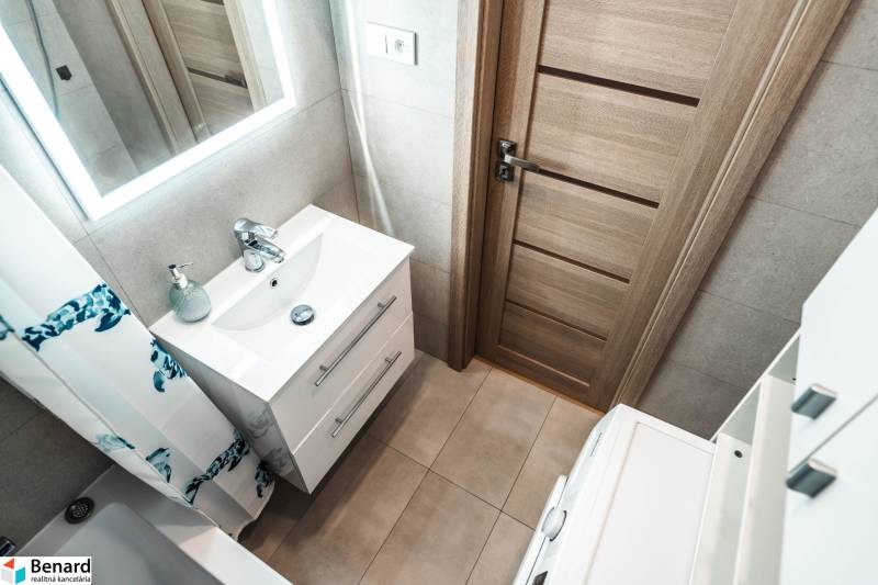 Fürdőszoba egy kétszobás lakásban mosdóval, tükörrel és faajtóval.