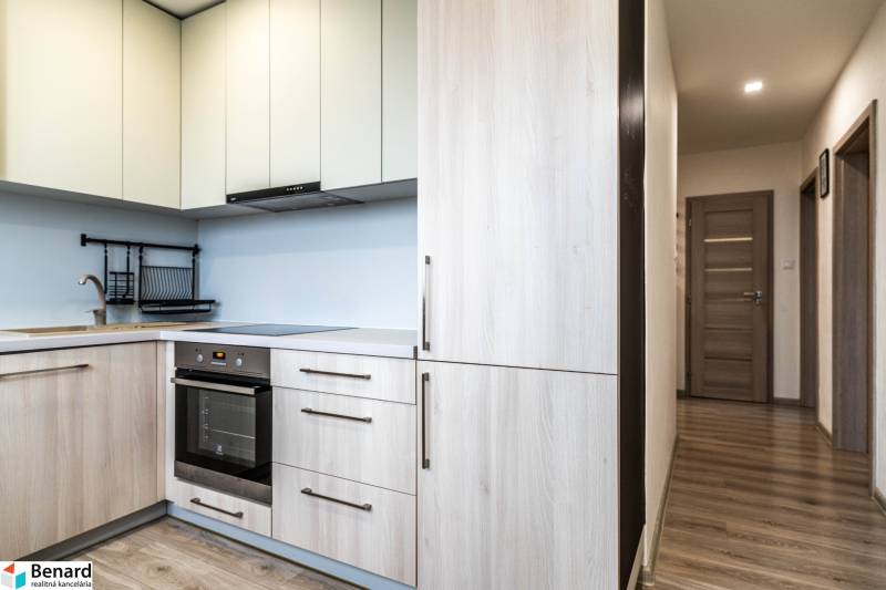 Konyha egy kétszobás lakásban, fa dekoros padlóval és világos szekrényekkel.