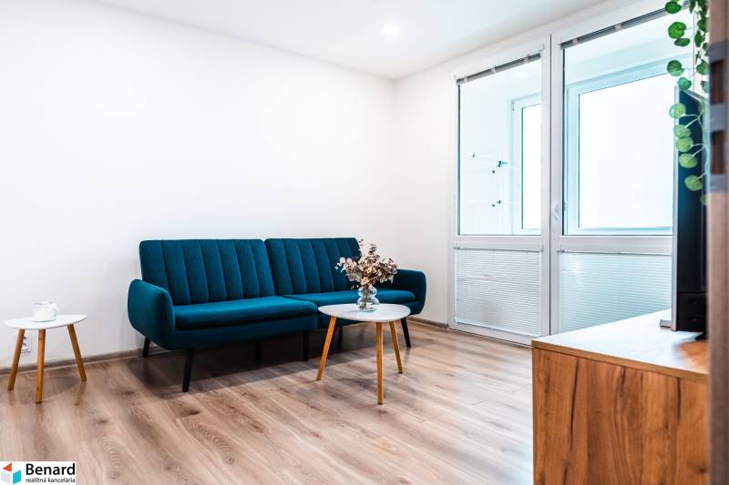 Nappali egy kétszobás lakásban kanapéval, fa mintázatú padlóval és dohányzóasztallal.