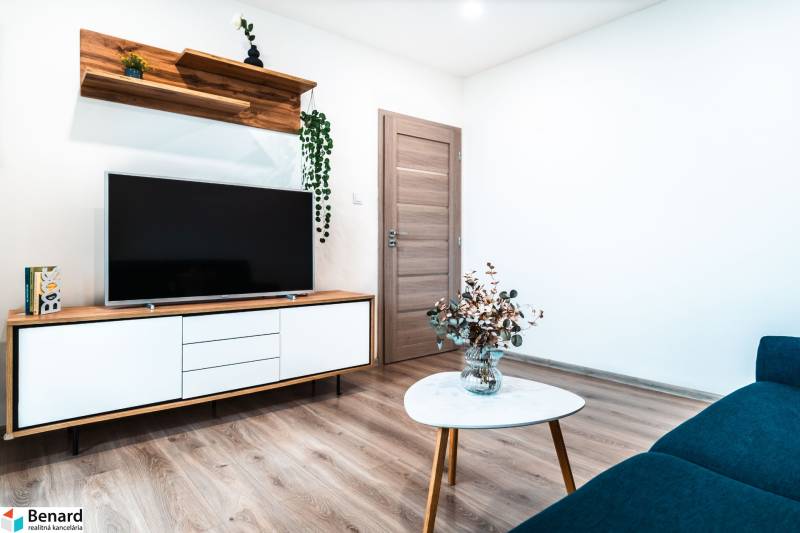 Nappali televízióval, szekrénnyel, zsámollyal és fa dekorációs padlóval egy kétszobás lakásban.