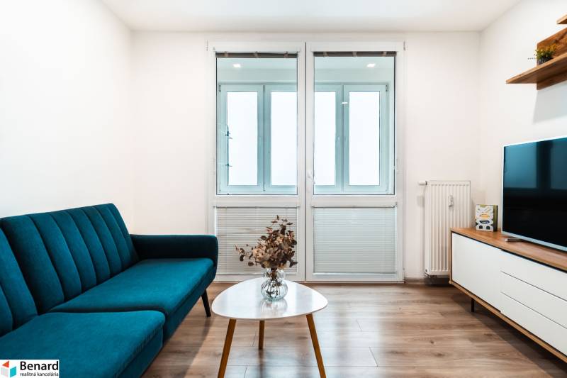 Nappali egy kétszobás lakásban kanapéval, televízióval és fa dekorációjú padlóval.