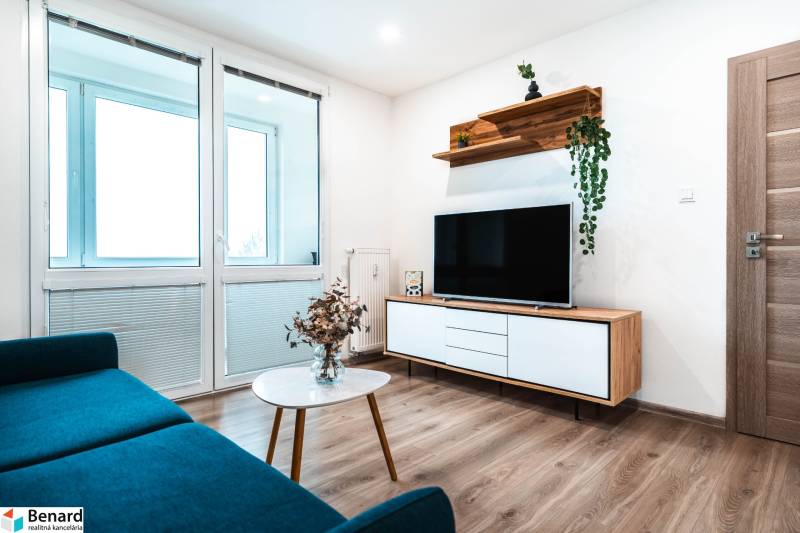 Nappali egy kétszobás lakásban kanapéval, televízióval és fa dekorációjú padlóval.