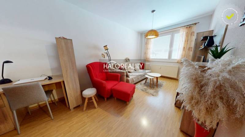 Nappali egy kétszobás lakásban, asztallal, piros fotellel és fa dekoros padlóval.