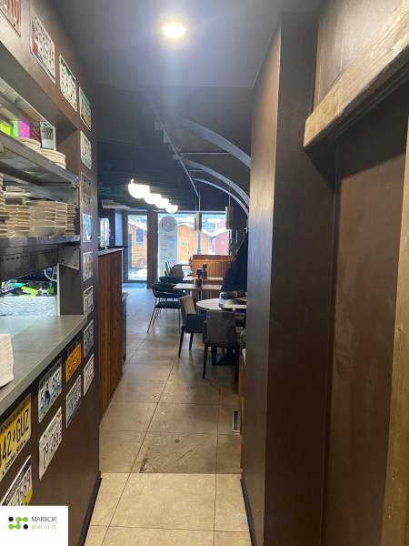 Vendéglátóhely belső tere polcokon tányérokkal, táblákkal, asztalokkal és székekkel.