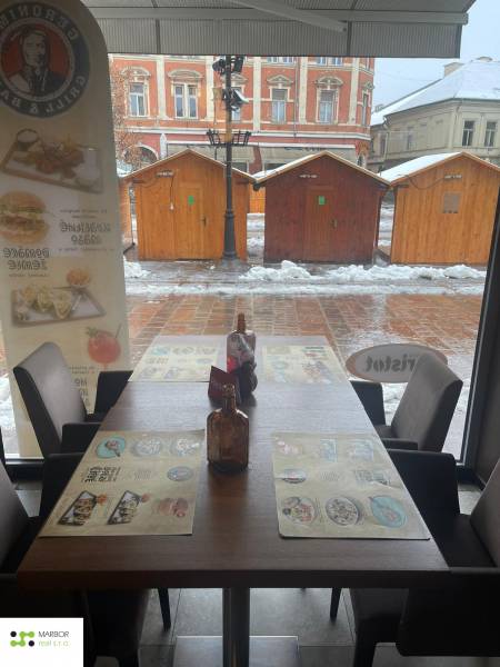 Téli táj az ablakon keresztül egy vendéglátóhelyen, kilátással a fából készült asztalokra.