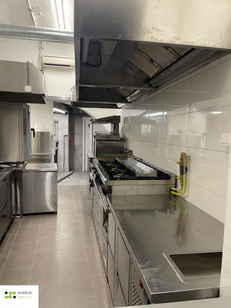 Professzionális konyha rozsdamentes acél készülékekkel és fehér csempékkel a vendéglátóipari helyiségekben.