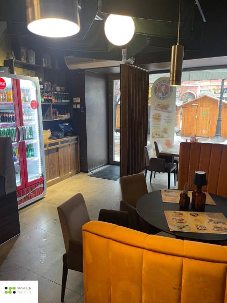 Gasztronómiai tér belső része kör alakú asztallal, székekkel és világítással.