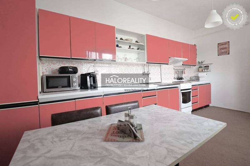 Konyha egy családi házban rózsaszín szekrényekkel és fehér asztallal.