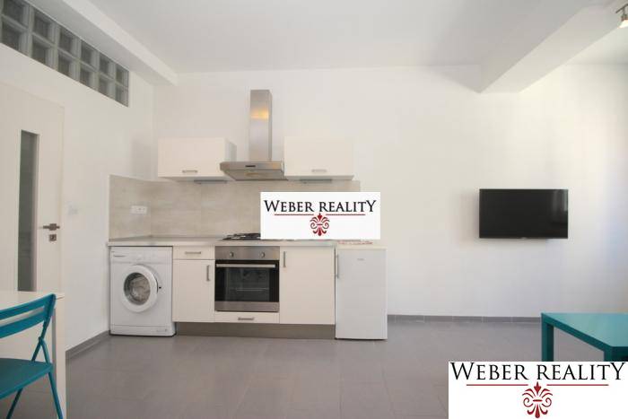 Konyha egy kétszobás lakásban fehér konyhabútorral, mosógéppel és falra szerelt televízióval.