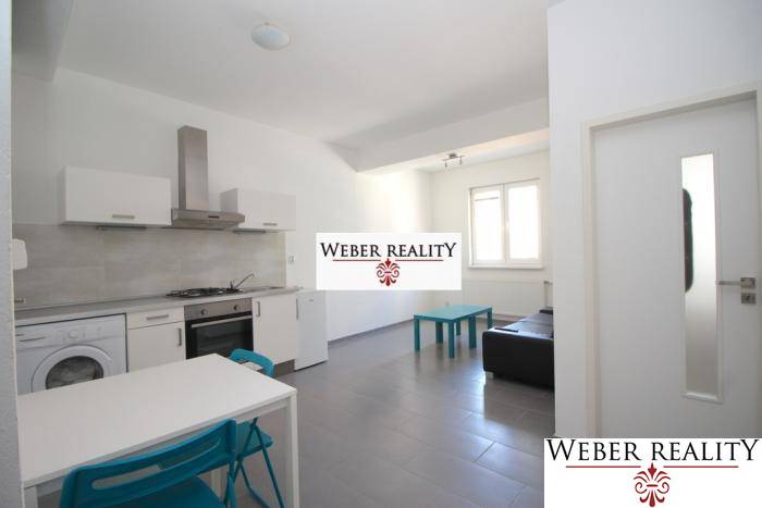 Nappali egy kétszobás lakásban konyhasarokkal, egyszerű berendezéssel és ablakkal.