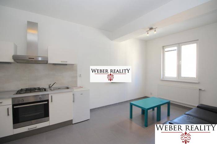 Konyha egy kétszobás lakásban szürke padlóval, konyhabútorral és ülőhellyel.