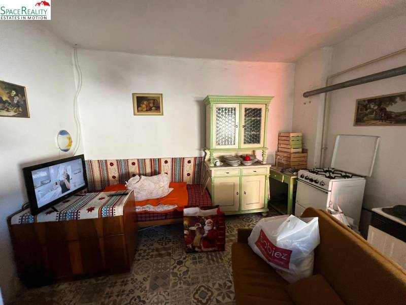 Szoba kanapéval, konyhapulttal, tűzhellyel és televízióval egy családi házban.